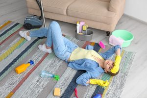 Tired Woman With Cleaning Supplies Lying On Carpet At Home